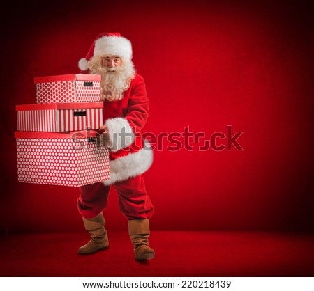 Photo of kind Santa Claus holding huge gift boxes and looking at camera. Full length portrait