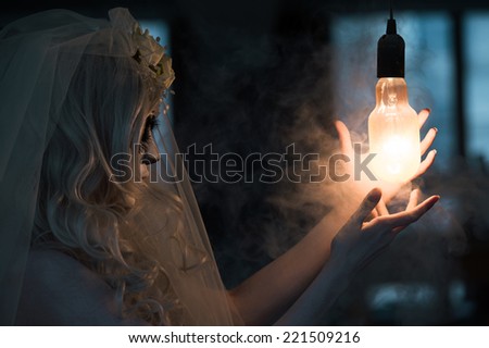 Halloween witch. Beautiful woman wearing santa muerte mask casting spell near light bulb
