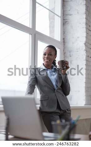 Happy african business woman enjoying the coffee break at her office and looking at window