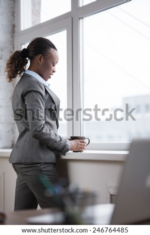 Happy african business woman enjoying the coffee break at her office and looking at window