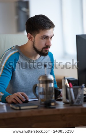 Businessman at work. Handsome young bearded man working on computer while sitting at his office