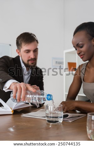 Caucasian businessman pouring water to his african colleague during the business meeting