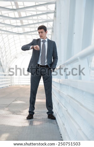 Businessman looking at watches while walking outside modern building