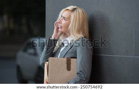 Successful businesswoman or entrepreneur talking on cellphone while standing outdoor. City business woman working.