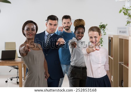 Group of friendly businesspeople with female leader in front pointing at camera