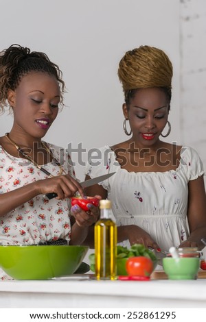 Two african women cooking in kitchen making healthy food salad with vegetables