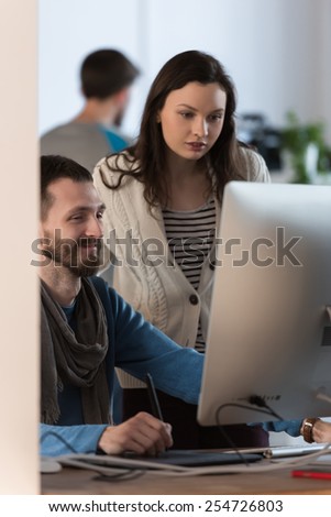 Artist or designer drawing something on graphic tablet at the office and discussing it with colleague