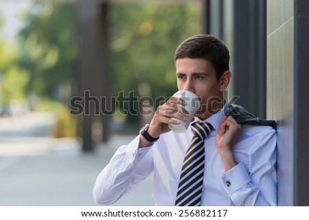 Portrait of a handsome businessman drinking coffee on the street near office building
