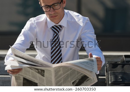 Well dressed business man reading newspaper sitting on a street sidewalk