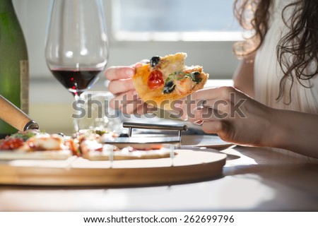 Beautiful young woman eating homemade pizza and drinking red wine at home
