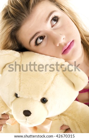 Young blond fashionable girl posing with teddy bear in studio isolated
