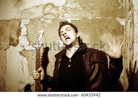 Young attractive man guitar player and singer inside empty room with old vintage wall. Halloween theme