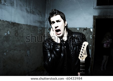 Young attractive man guitar player and singer inside empty room with old vintage wall