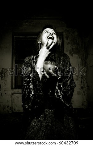 Young emotional gothic woman hanging candle in empty grunge dark room. Halloween theme