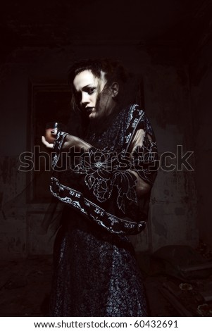 Young emotional gothic woman hanging candle in empty grunge dark room. Halloween theme