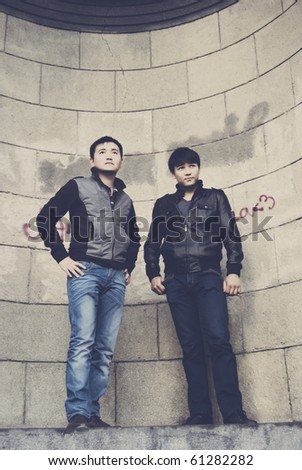 Portrait of a two modern handsome asian men against vintage wall of old building