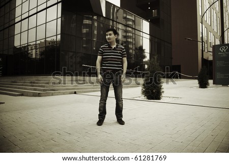 Dramatic portrait of young asian man against modern glass wall of skyscraper