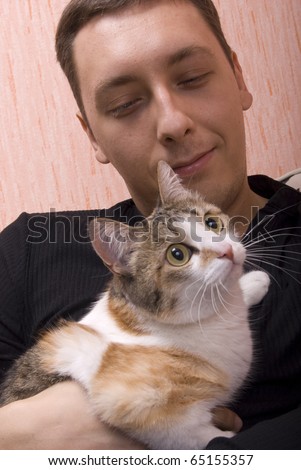 Young attractive man playing with his cat on sofa in his apartment
