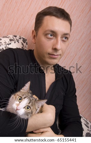 Young attractive man playing with his cat on sofa in his apartment