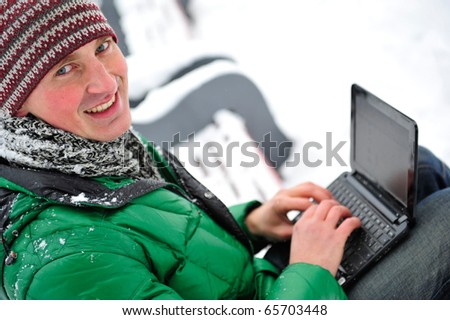 Closeup portrait of young handsome man in sportswear working on his laptop outdoor sitting on bench in winter park. Healthy lifestyle
