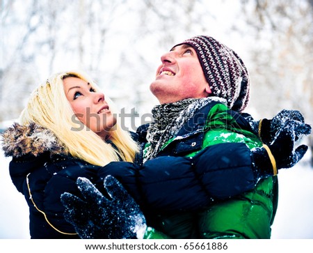 Happy couple of male and female embracing and having fun wearing warm clothes outside in winter park on snowdrift