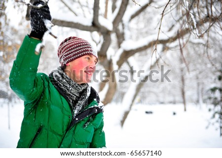 Portrait of young cheerful man outdoor in winter park holding tree branch