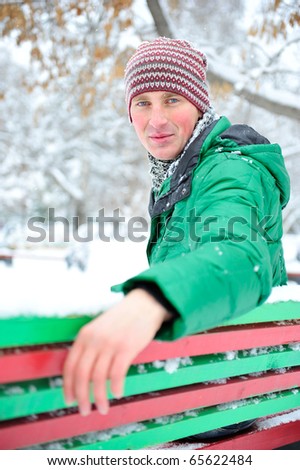 Portrait of young man outdoor resting on bench in winter park