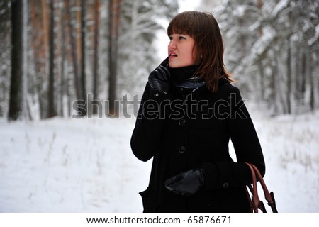 Outdoor portrait of young beautiful european style woman - walking through the winter forest wearing black coat and leather gloves