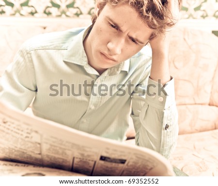 Portrait of young handsome guy reading newspaper in his apartment at night