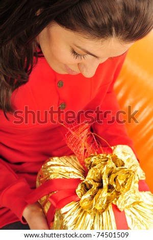 Beautiful happy woman on an orange sofa holding a gift in her arms