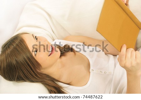 Closeup portrait of beautiful young brunette woman on the bed at home. Reading book