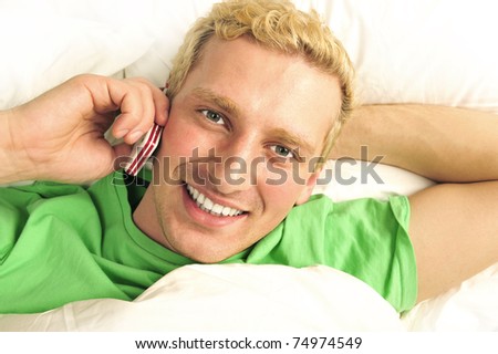 A man in his bed speaking cell phone and looking at camera