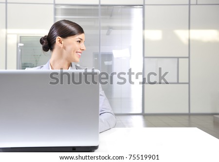 Beautiful happy and smiling business woman working on computer at her office and looking right from the camera