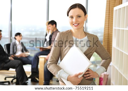 Closeup portrait of pretty cheerful business woman in an office environment holding laptop. Large panoramic window on background