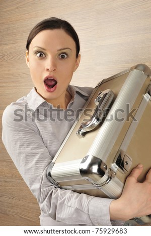 Portrait of emotional pretty young woman against modern stylish wooden wall holding big metal case. Screaming with open mouth