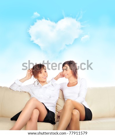 Portrait of two young pretty girls sitting relaxed on sofa discussing their relations with boys