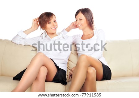 Portrait of two young pretty girls sitting relaxed on sofa and talking about something isolated on white background