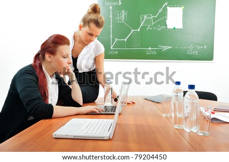 Portrait of two young business women at their office working near desk using papers laptop board microphone water and other tools