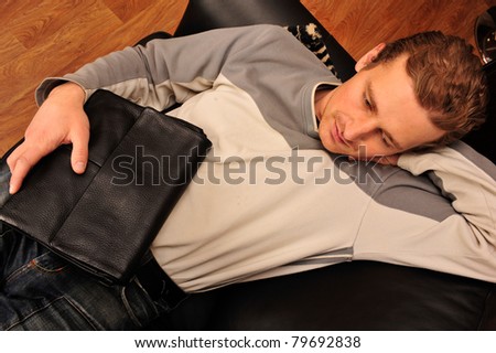 Happy young man sitting on sofa at home and holding handbag