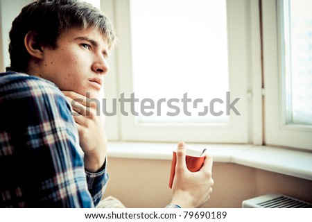 Happy young handsome man at home, drinking coffee or tea near window