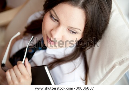 Young sexy woman at home reading book sitting in comfortable armchair near big window