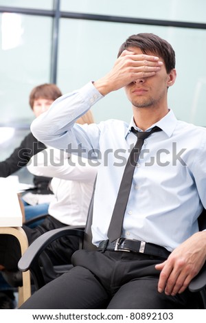 Closeup portrait of a smart young businessman with closed eyes and his colleagues working at the back