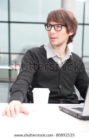 Friendly executive sitting in front of laptop in his office. Big window at the background. Looking away, daydreaming