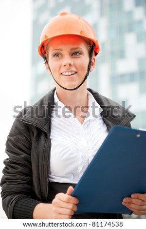 Young architect-woman wearing a protective helmet standing on the building background