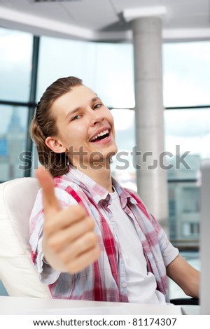 Happy satisfied young man sitting relaxed on his armchair and thumbs up to camera - Indoors