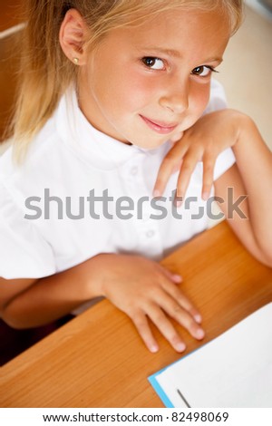 Image of smart child reading interesting book in classroom. Vertical Shot. Looking at camera