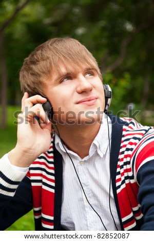 Student outside sitting on green grass daydreaming and listening music via his player and headphones