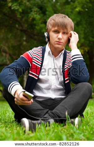 Student outside sitting on green grass and listening music via his player and headphones