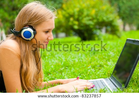 A smiling young girl with laptop outdoors listening music by headphones