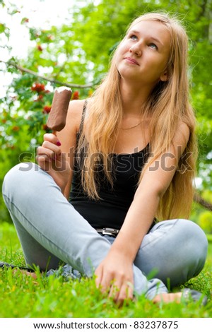Portrait of young woman eating ice-cream while sitting relaxed on green grass, sunny day outdoors